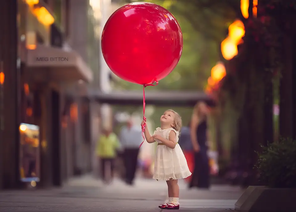 toddler-girl-holding-a-giant-red-balloon-by-Meg-Bitton.webp