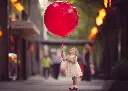 toddler-girl-holding-a-giant-red-balloon-by-Meg-Bitton.webp